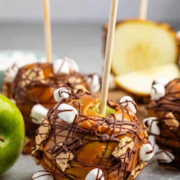 green apple dipped in caramel and chocolate with marshmallows and graham cracker stuck to side.