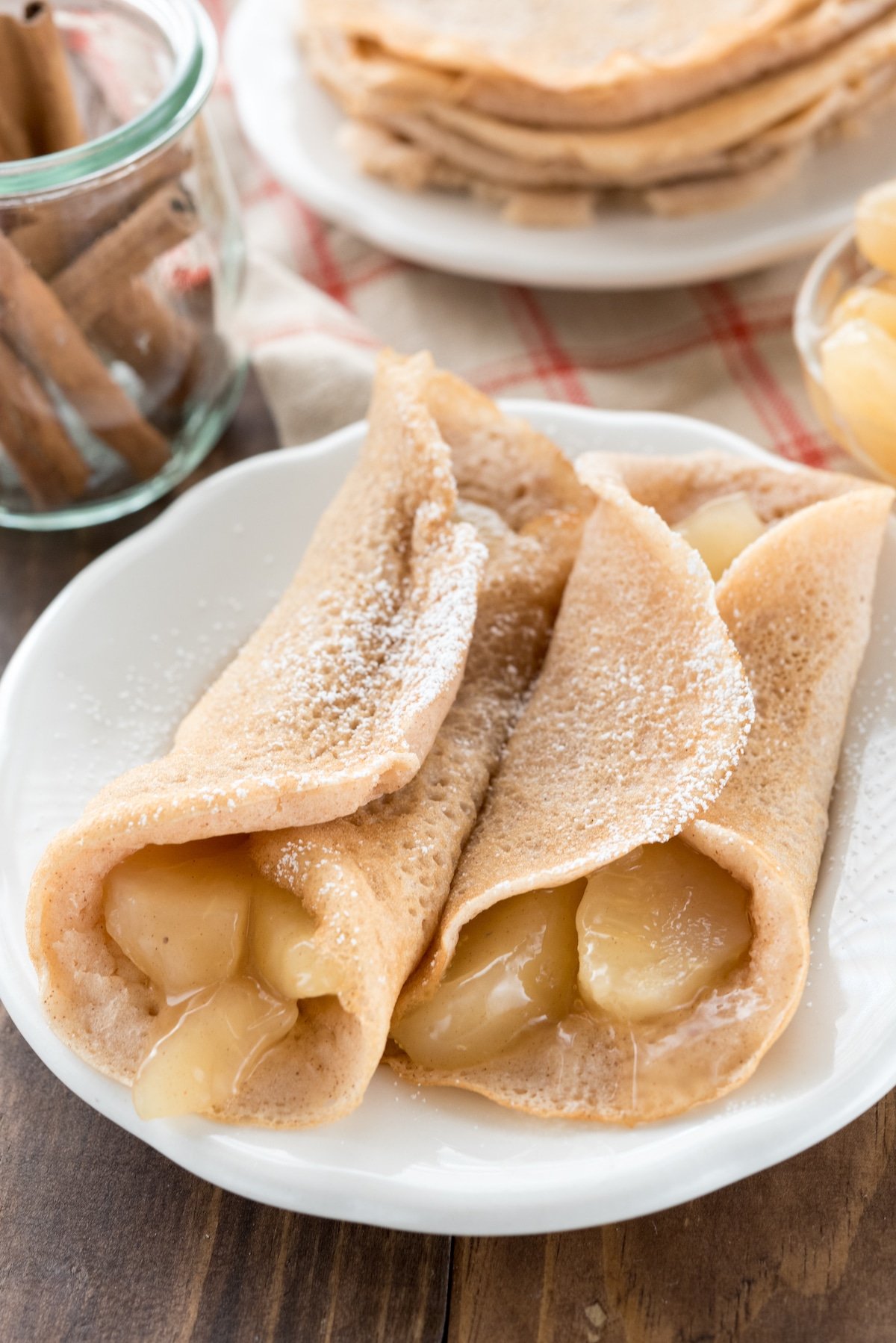 apples rolled up in pancakes on a white plate with powdered sugar on top.