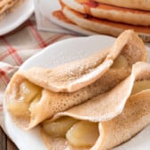 apples rolled up in pancakes on a white plate with powdered sugar on top.