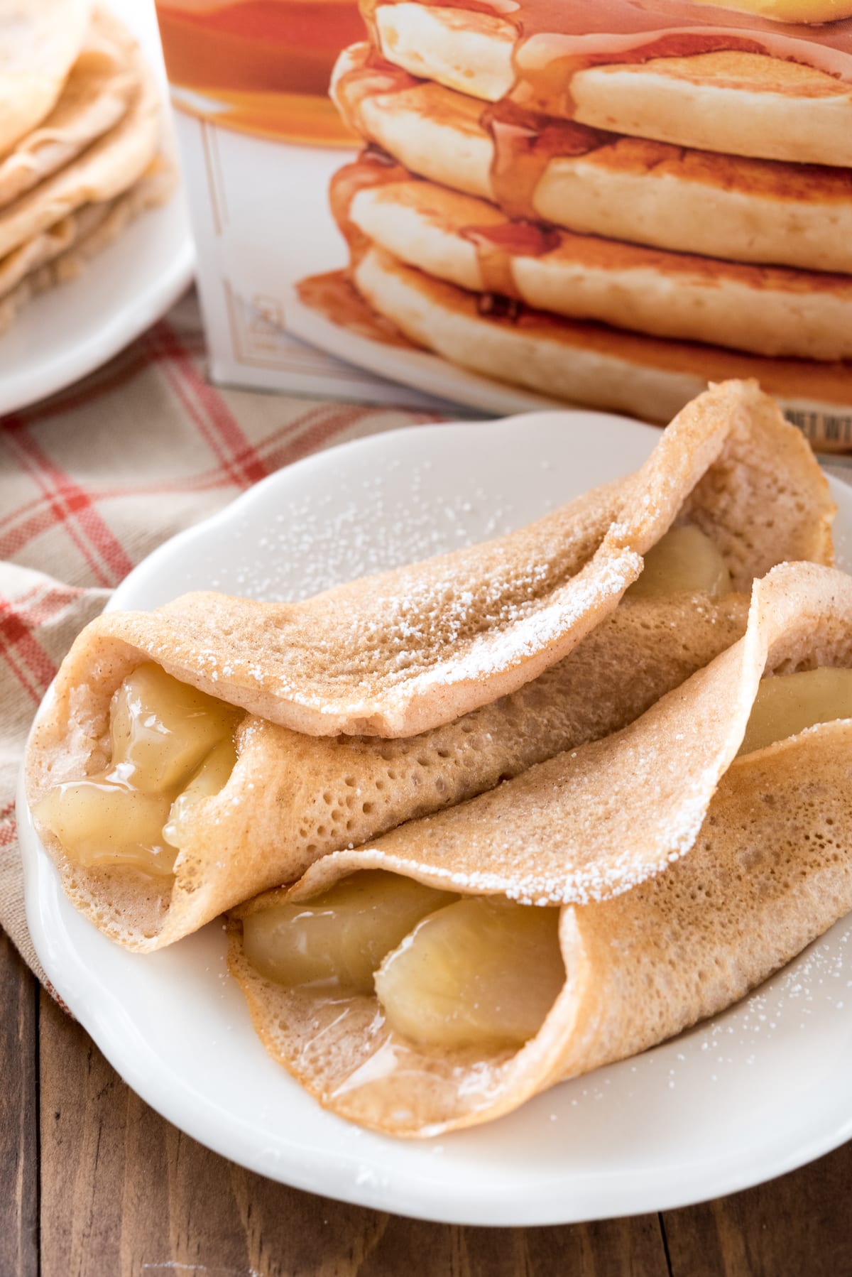 apples rolled up in pancakes on a white plate with powdered sugar on top.