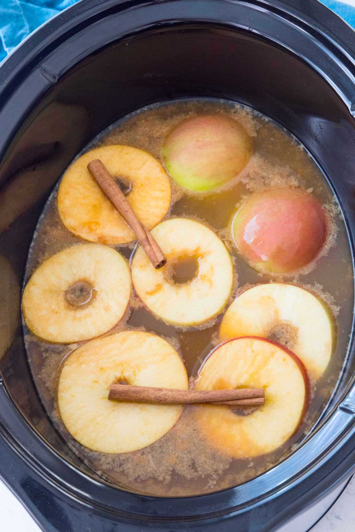 sliced apples and cinnamon sticks in a black crockpot.
