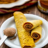 pumpkin pancakes rolled up on a white plate.