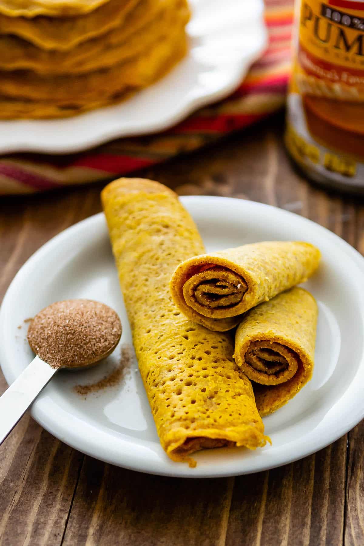 pumpkin pancakes rolled up on a white plate.