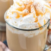 latte in a clear glass with whipped cream and caramel on top.