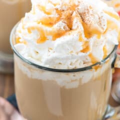 latte in a clear glass with whipped cream and caramel on top.