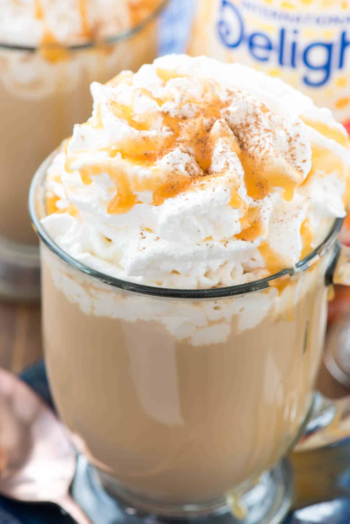 latte in a clear glass with whipped cream and caramel on top.