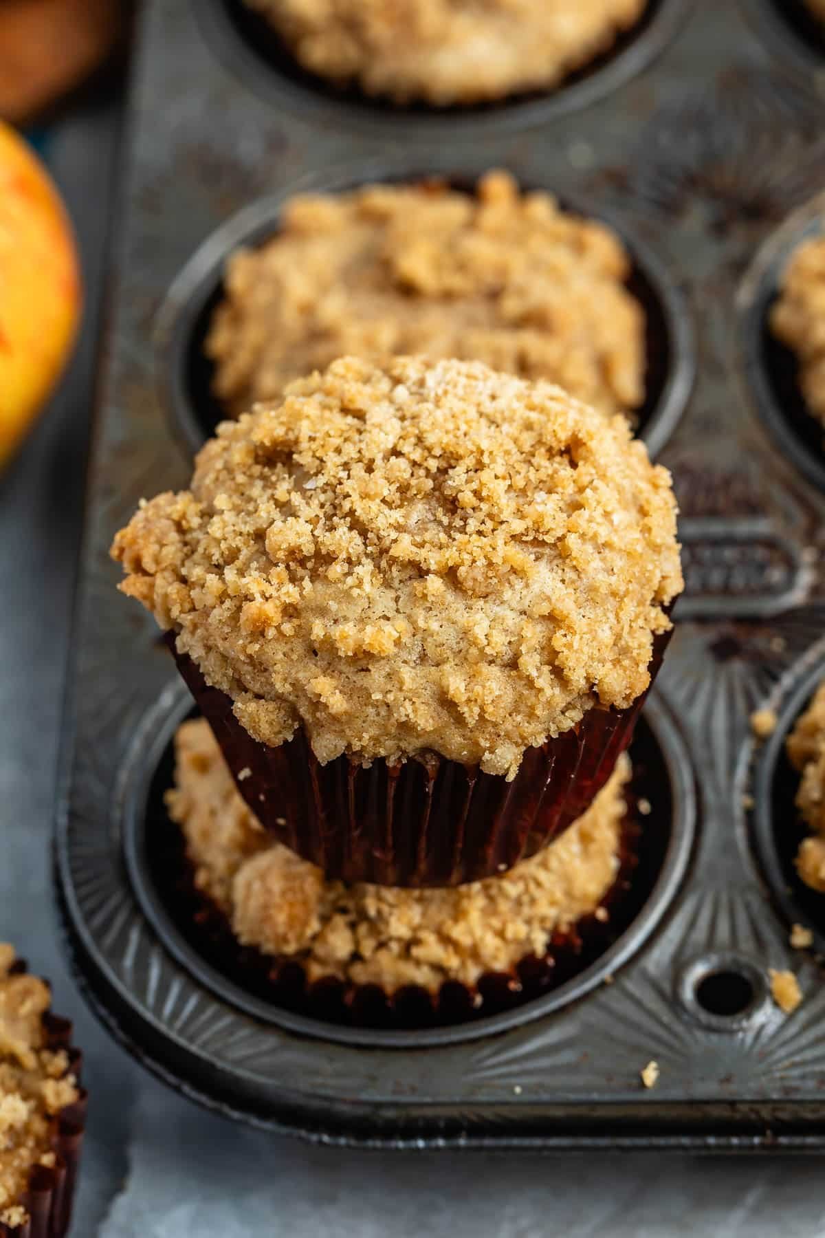 apple muffins in a brown cupcake tin with a crumble topping.