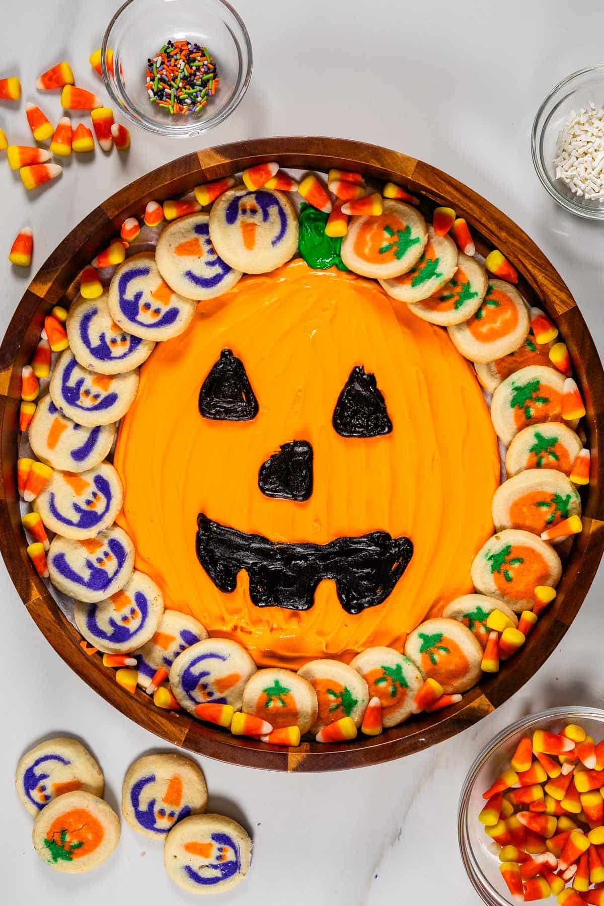 frosting board with pumpkin decorations and pumpkin cookies around it.