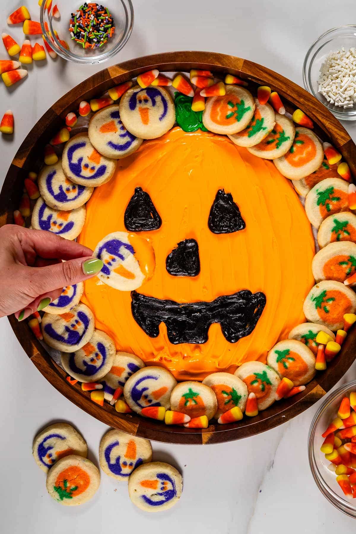 frosting board with pumpkin decorations and pumpkin cookies around it.