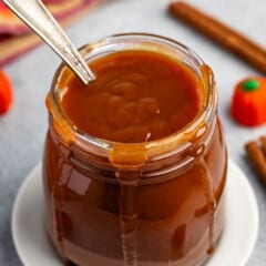 caramel in a clear jar with a spoon scooping it.