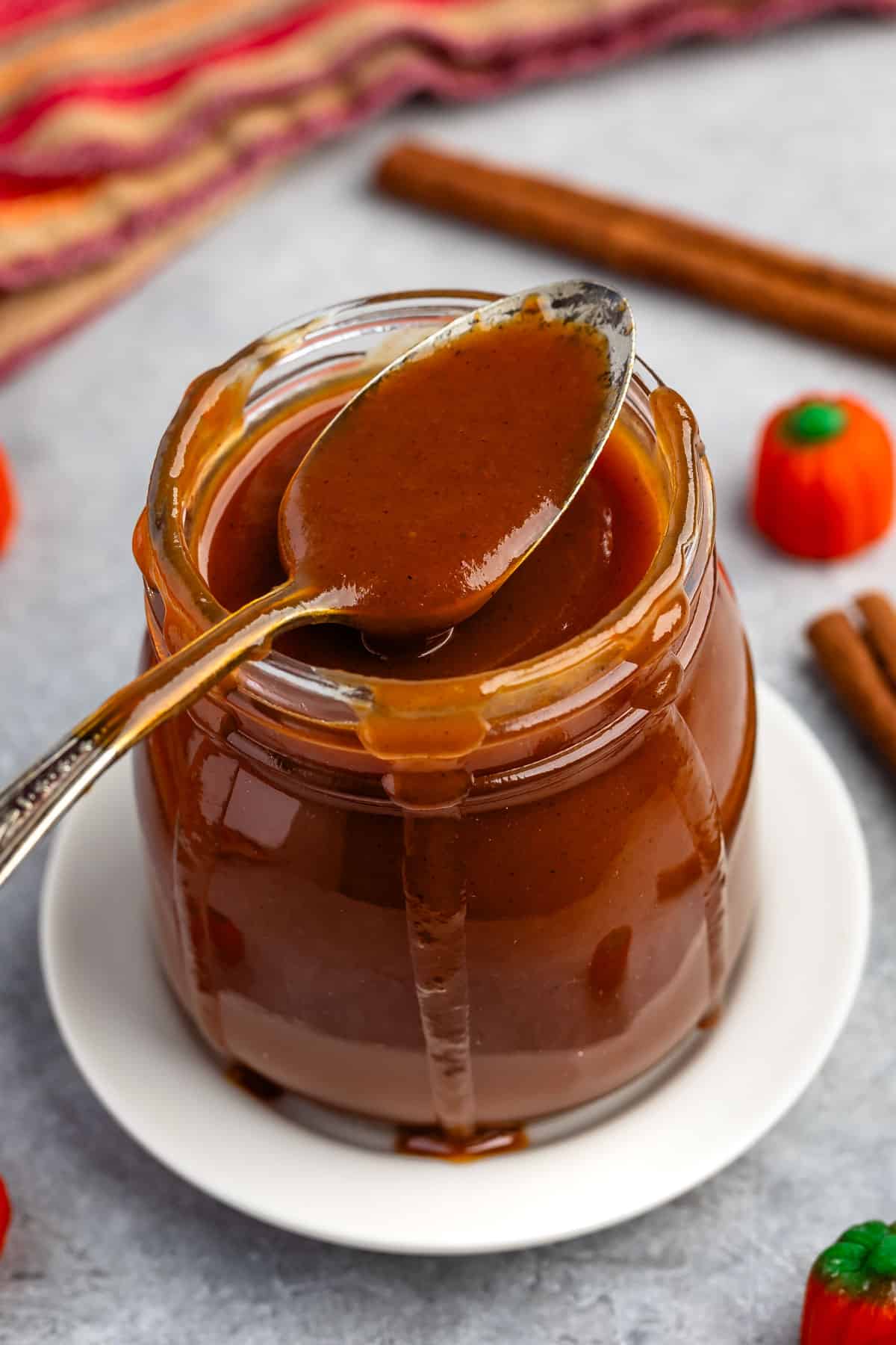 caramel in a clear jar with a spoon scooping it.