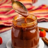 caramel in a clear jar with a spoon scooping it.