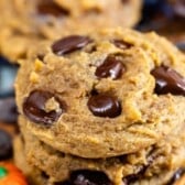 Close-up of two stacked pumpkin chocolate chip cookies on a wooden surface, with melted chocolate chips visible and a small decorative pumpkin nearby.