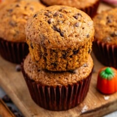 stacked muffins on a brown cutting board.