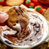 hand holding cookie that's being dipped into a white and brown dip.