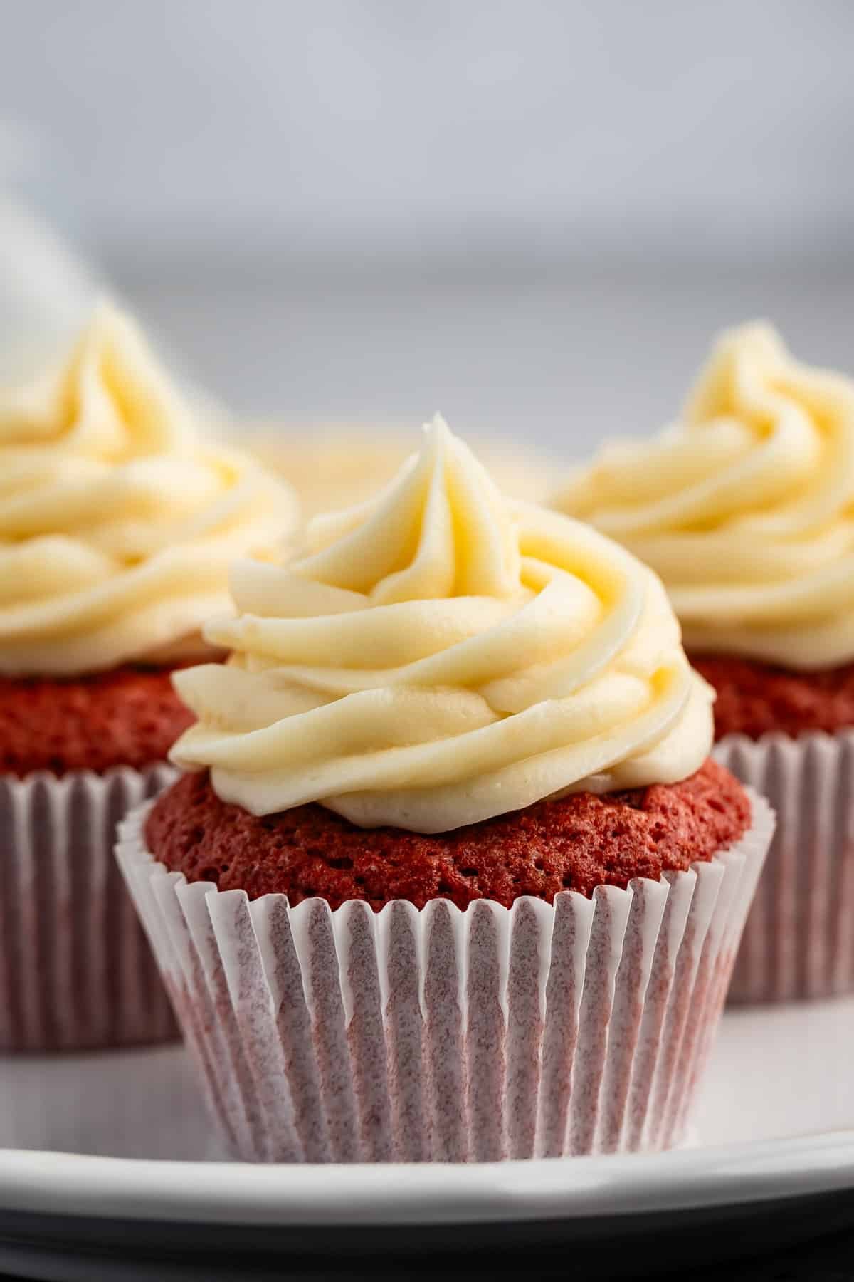 red cupcakes with frosting on top on a white plate.