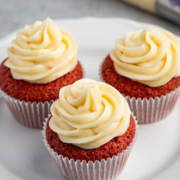 red cupcakes with frosting on top on a white plate.