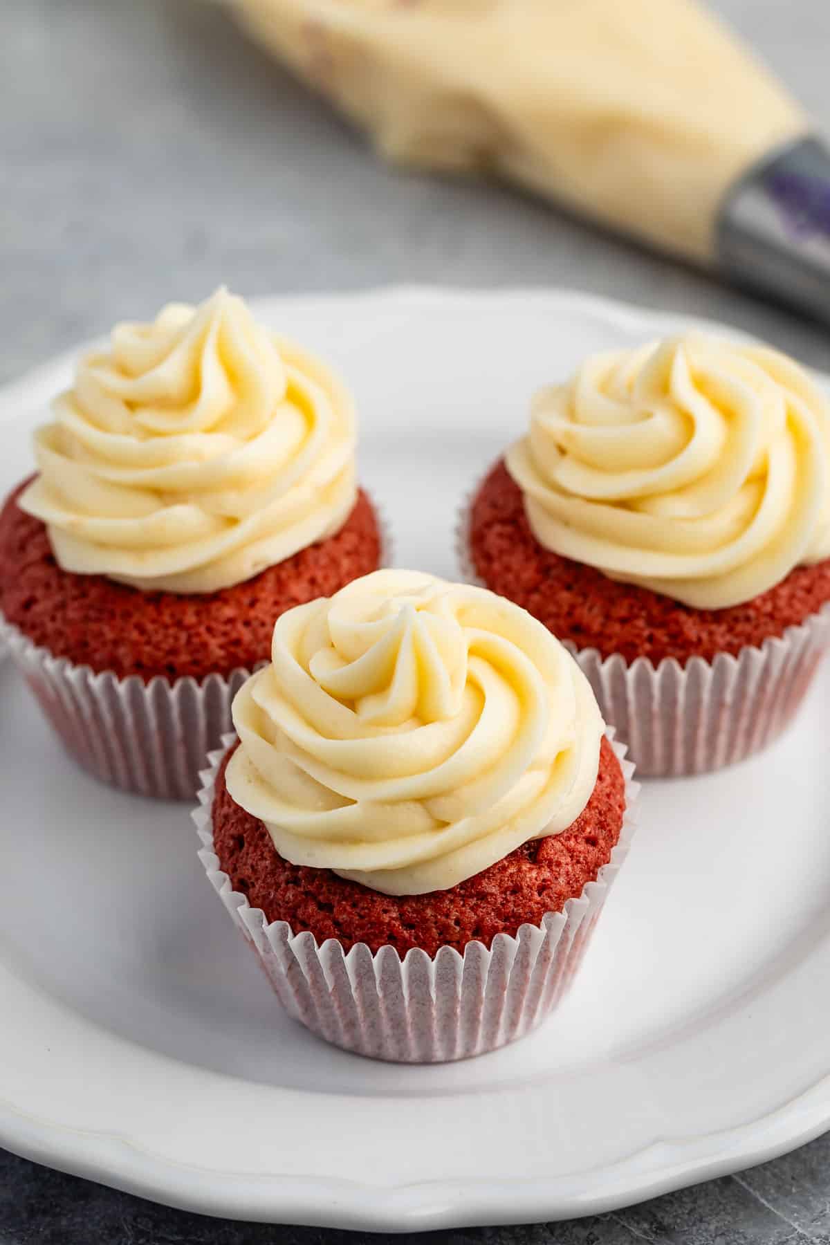 red cupcakes with frosting on top on a white plate.