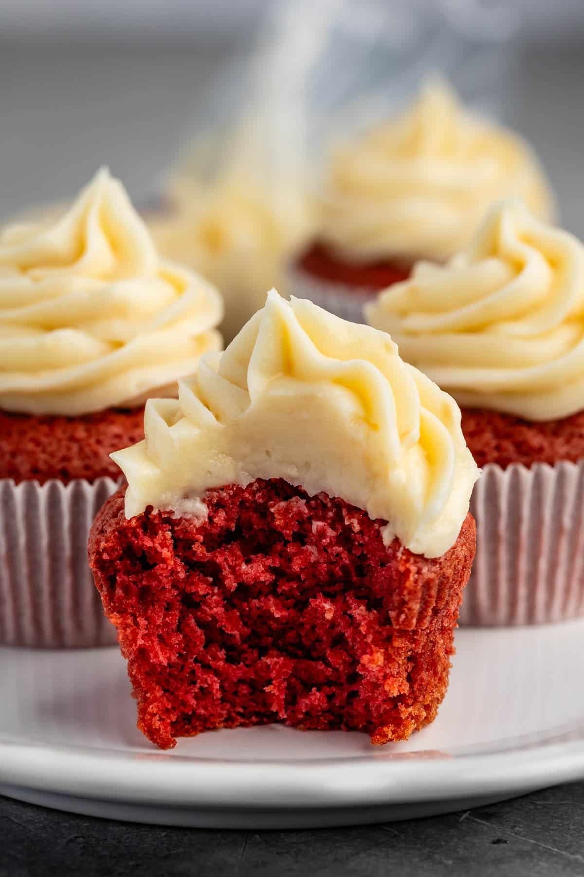 red cupcakes with frosting on top on a white plate.