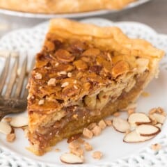 one slice of pie on a white plate with sliced almonds all around.