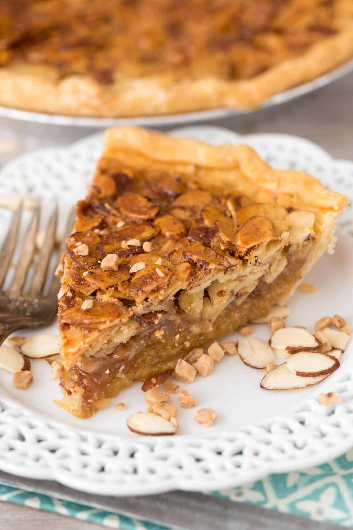 one slice of pie on a white plate with sliced almonds all around.