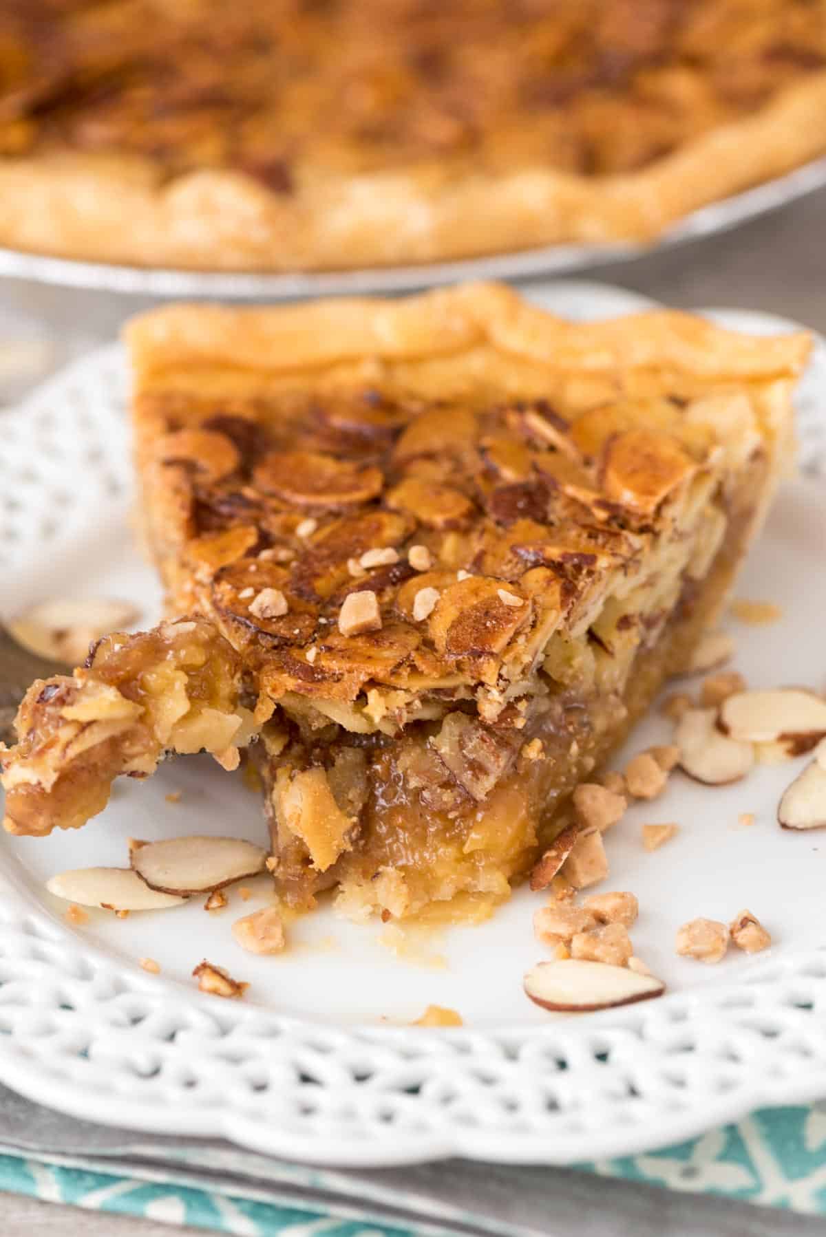 one slice of pie on a white plate with sliced almonds all around.