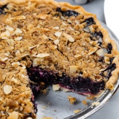blueberry pie in a clear plate with crumble on top.