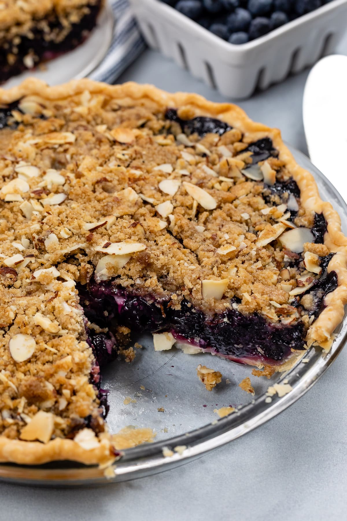 blueberry pie in a clear plate with crumble on top.