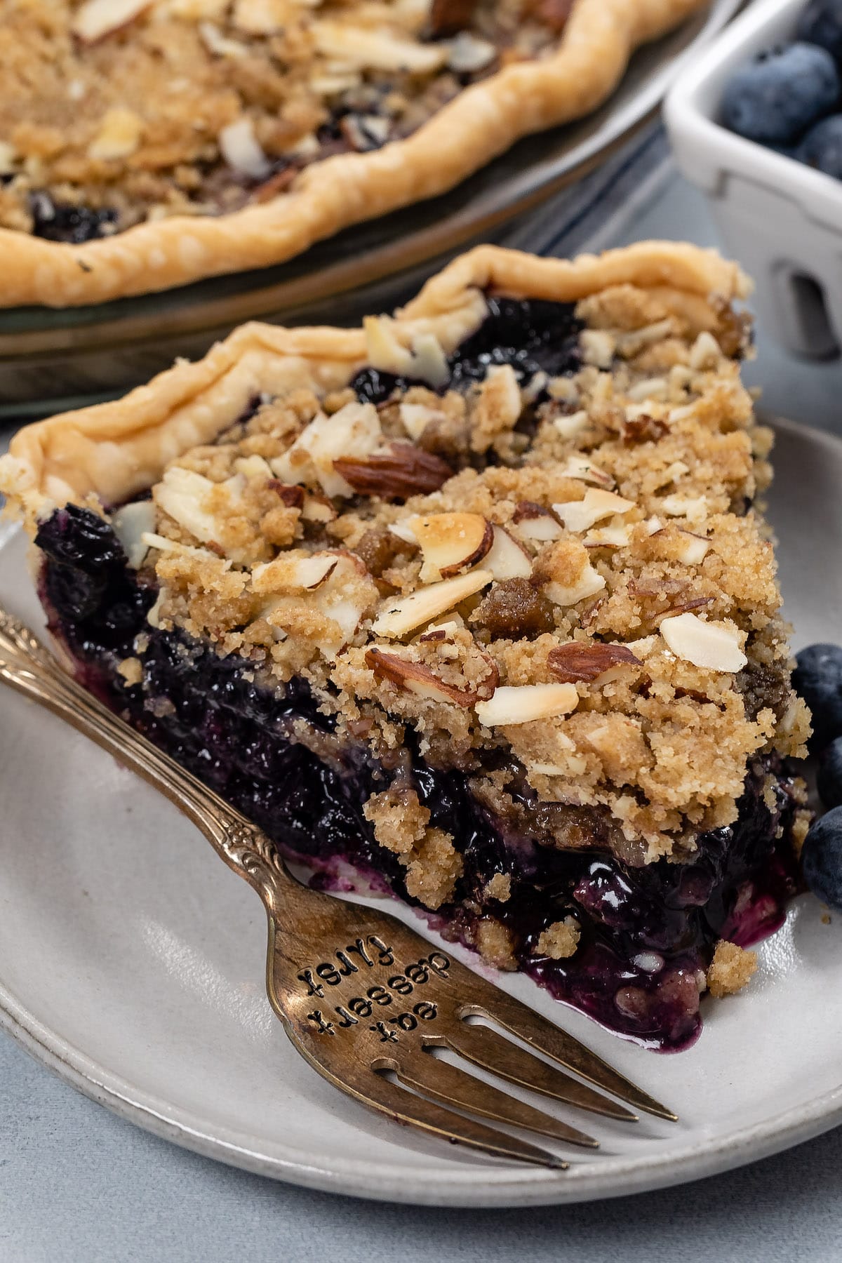 blueberry pie in a grey plate with crumble on top.