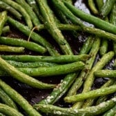 greens beans piled on each other on a black cooking sheet.