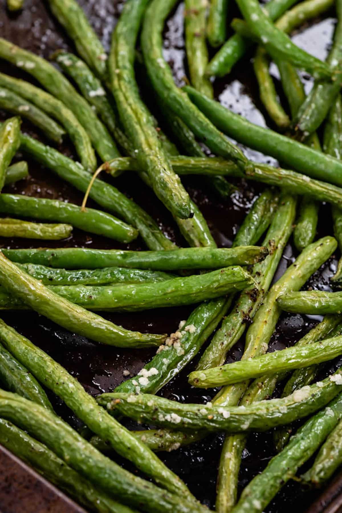 greens beans piled on each other on a black cooking sheet.