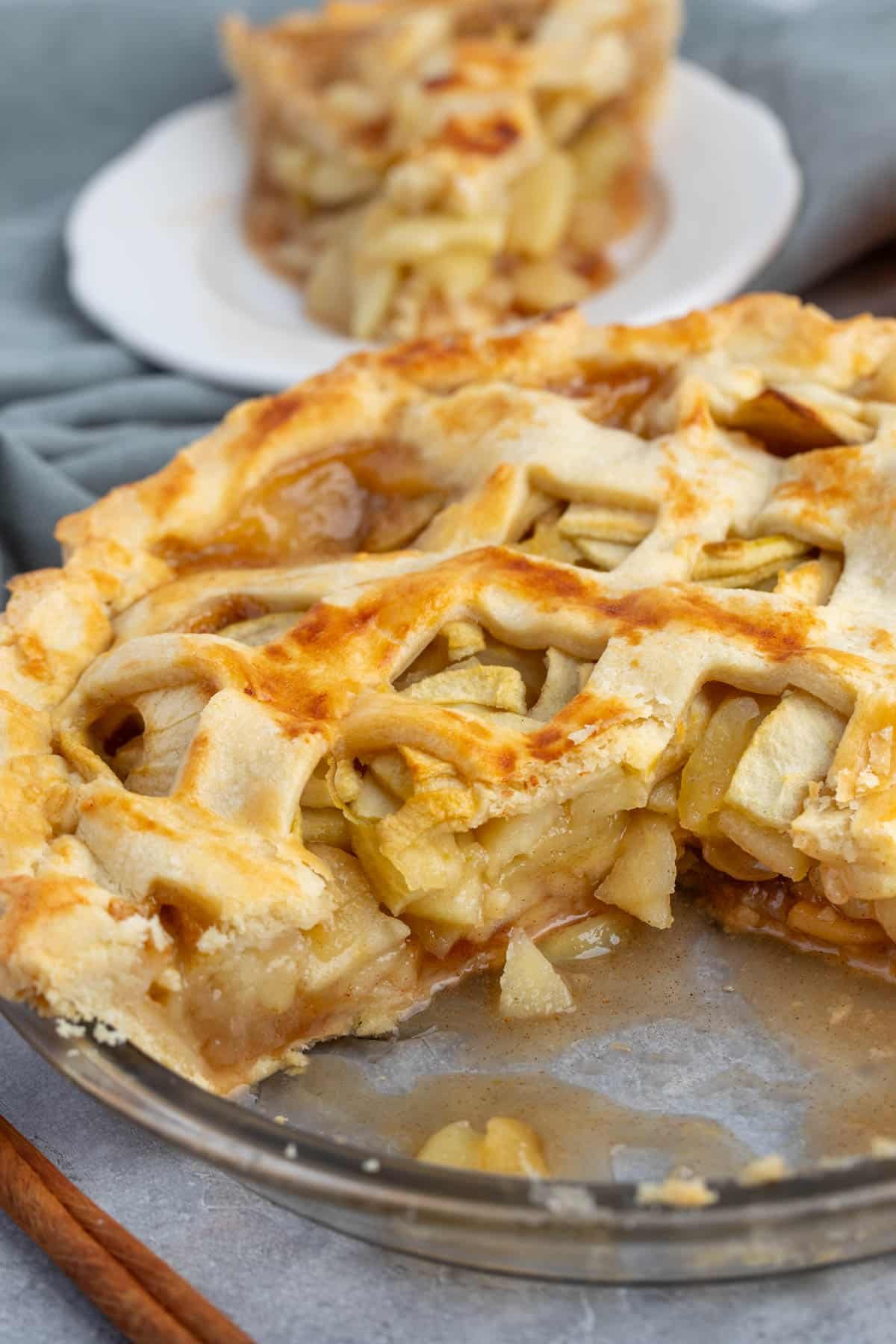 apple pie on in a clear glass pie plate with a sliced taken out.