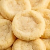 A close-up of several golden, round sugar cookies with slightly cracked surfaces, stacked on top of each other—these delicious treats are made from an easy sugar cookie recipe.
