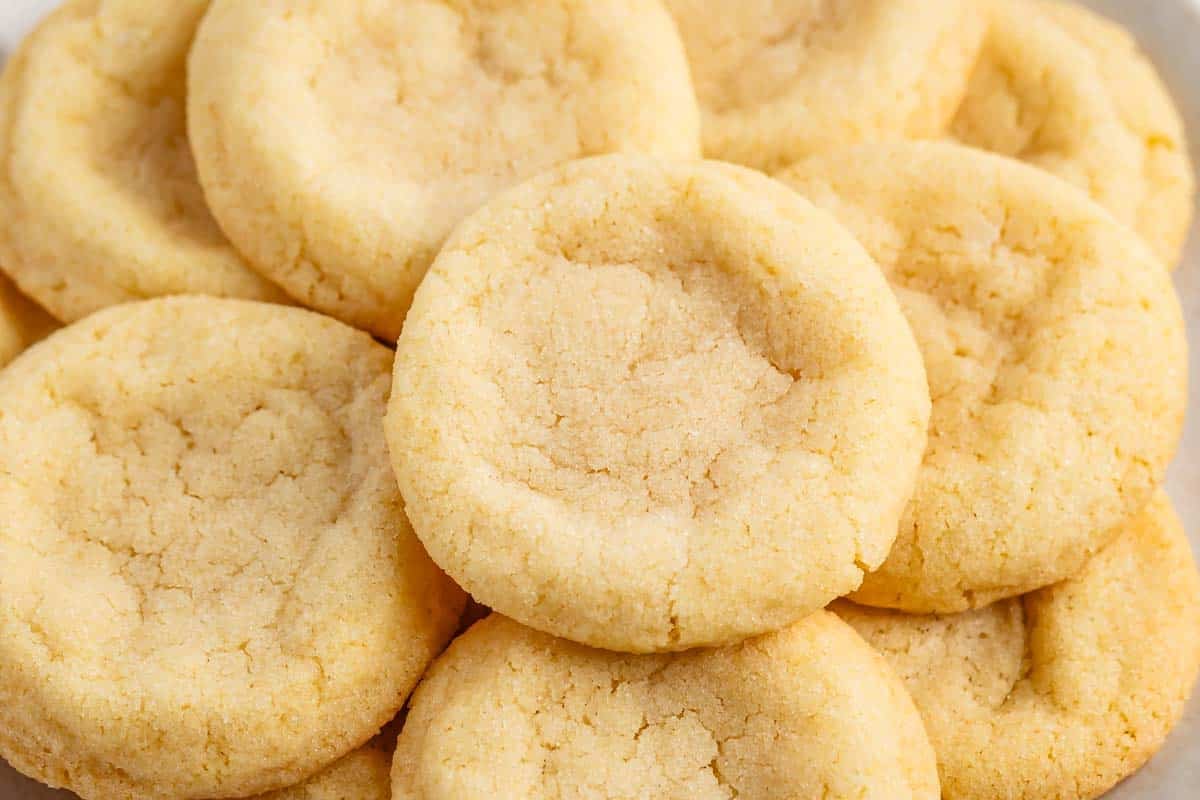A close-up of several golden, round sugar cookies with slightly cracked surfaces, stacked on top of each other—these delicious treats are made from an easy sugar cookie recipe.