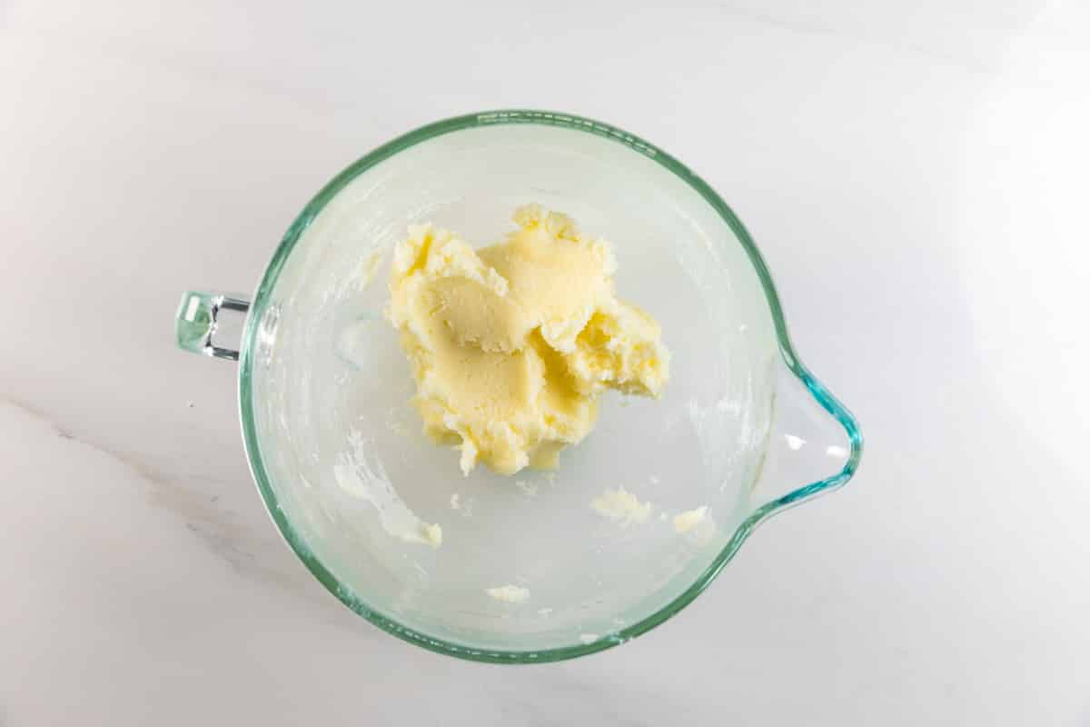 Un bol à mélanger en verre contient une petite quantité de beurre crème sur une surface blanche, prêt pour cette recette facile de biscuits au sucre.