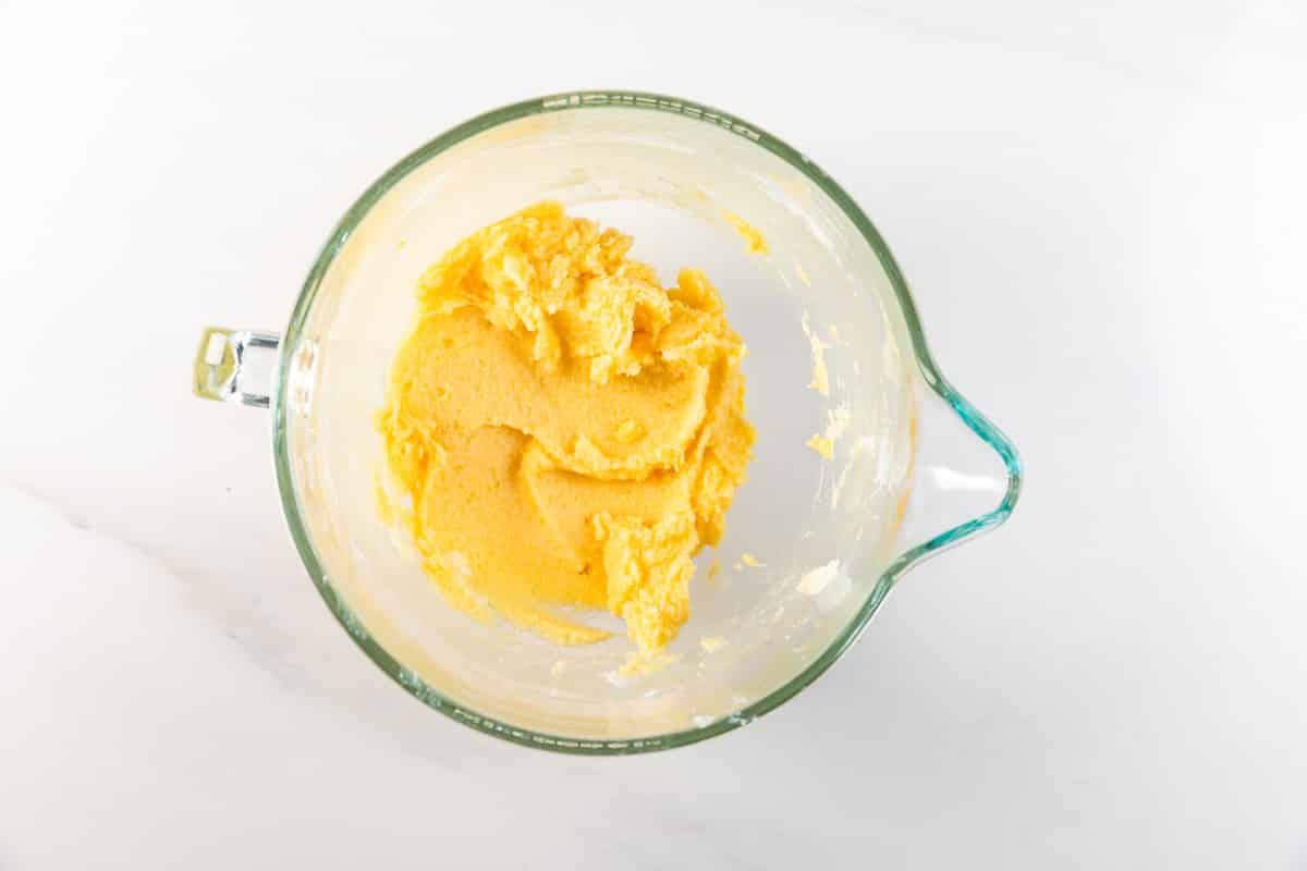 Un bol à mélanger en verre avec un mélange de pâte à biscuits jaune, fabriqué à partir d'une recette facile de biscuits au sucre, repose sur une surface blanche, vu de dessus.