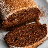 brown cake roll on a white plate with brown and white sugar sprinkled over the top of the roll.