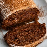 brown cake roll on a white plate with brown and white sugar sprinkled over the top of the roll.