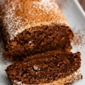 brown cake roll on a white plate with brown and white sugar sprinkled over the top of the roll.