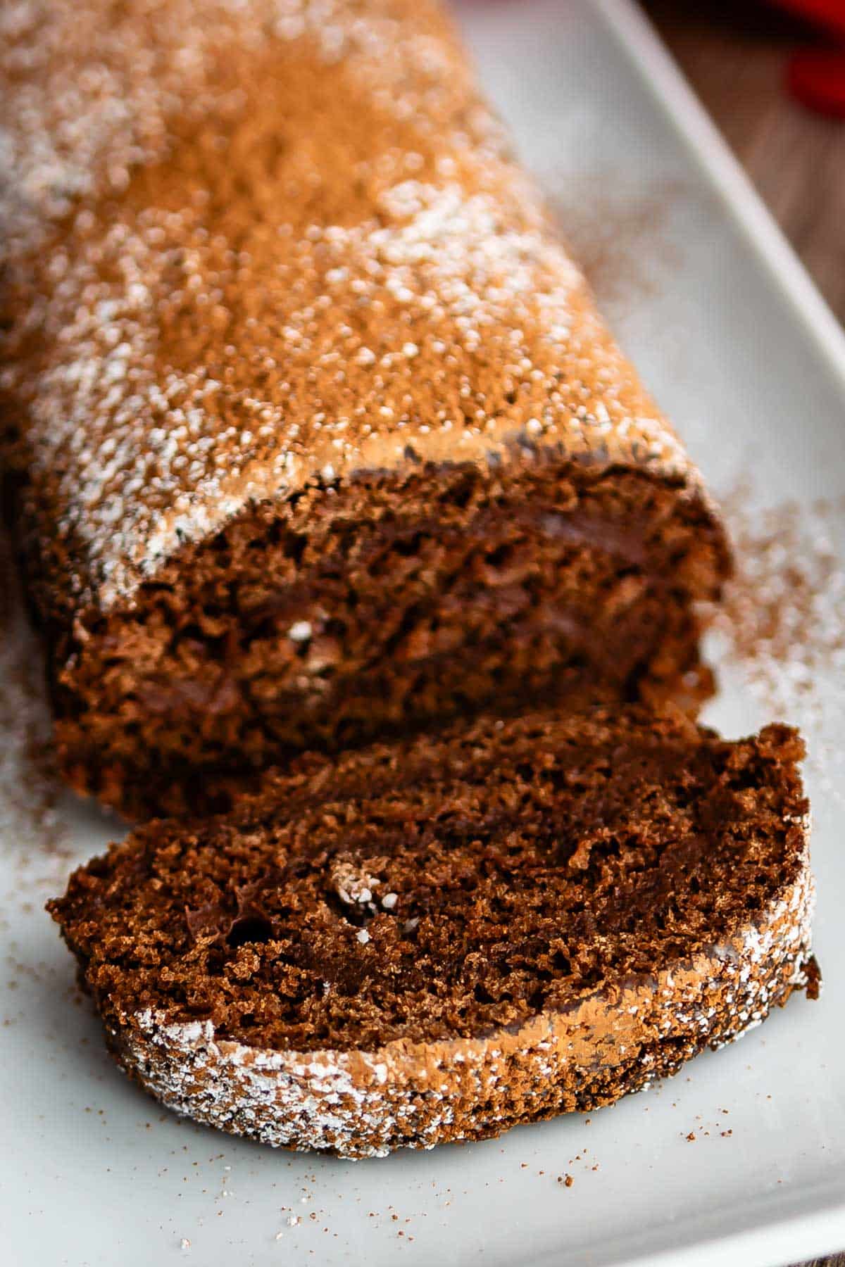 brown cake roll on a white plate with brown and white sugar sprinkled over the top of the roll.
