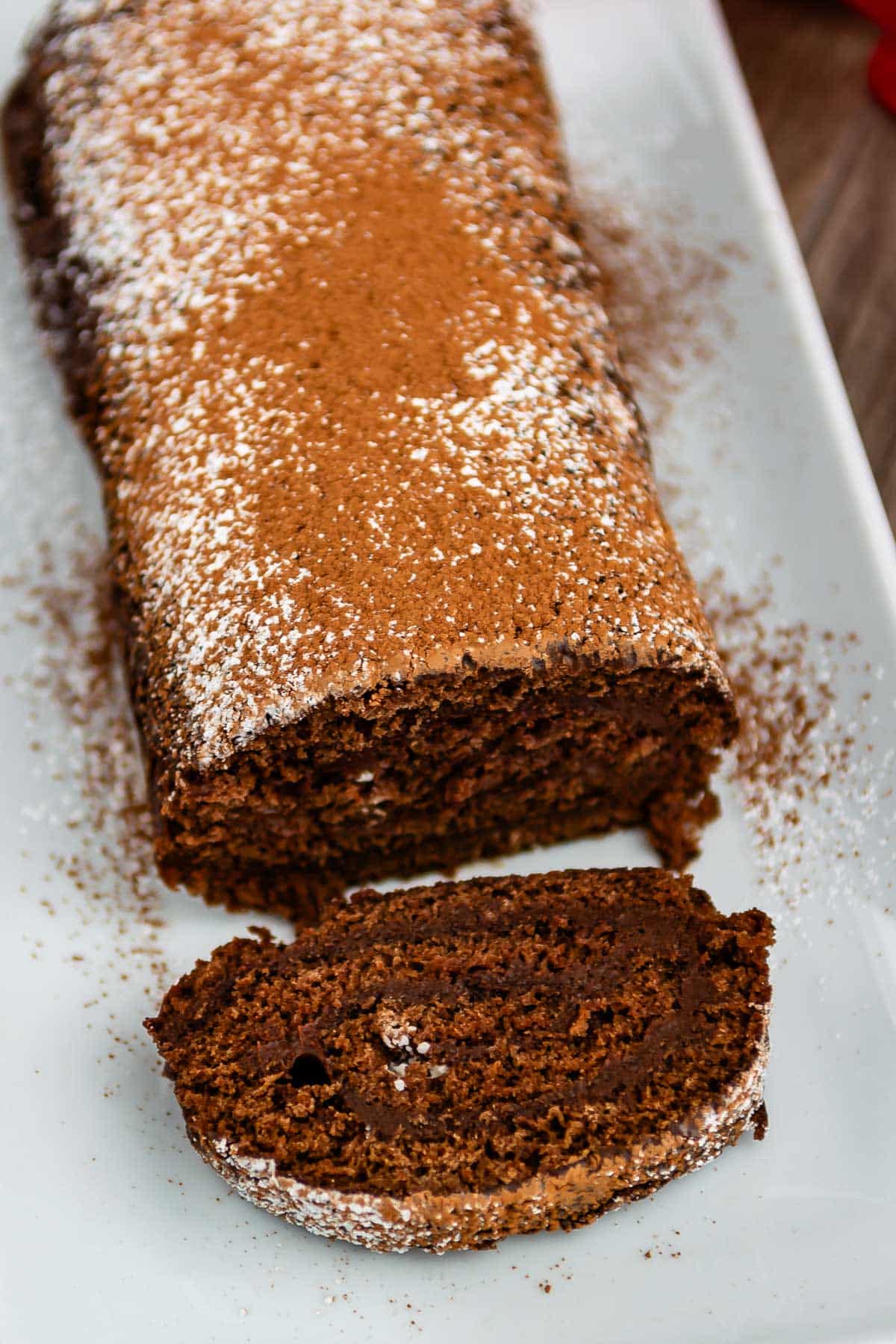 brown cake roll on a white plate with brown and white sugar sprinkled over the top of the roll.