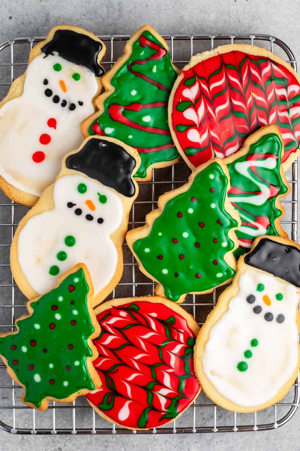 stacked christmas cookies in shapes like trees and snowmen with correlating frosting.