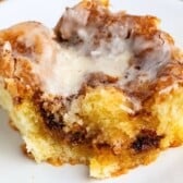 A close-up of a Cinnamon Roll Cake slice with swirls of cinnamon sugar, topped with creamy white glaze, served on a white plate.