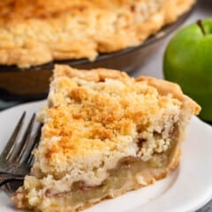 one slice of pie with crumble topping on a white plate next to a fork.