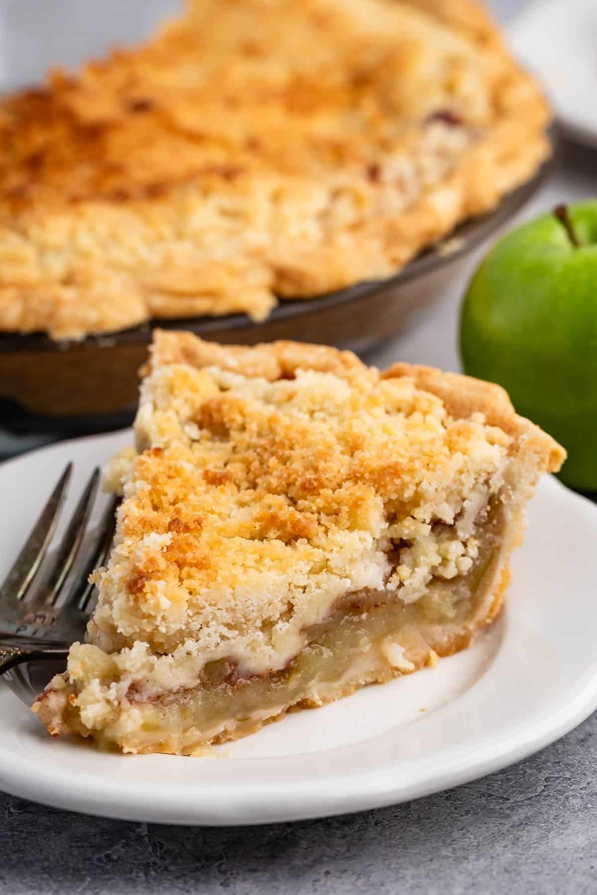 one slice of pie with crumble topping on a white plate next to a fork.