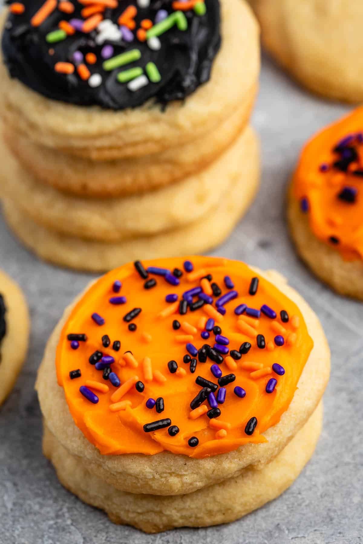 stacked sugar cookies with orange frosting and orange and purple sprinkles.
