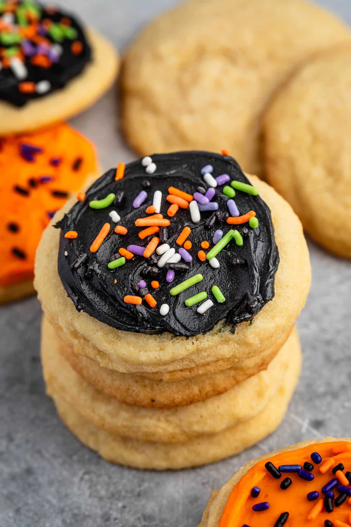 stacked sugar cookies with black frosting and orange and green sprinkles.