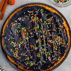 halloween pumpkin cookie cake with black frosting and sprinkles on top.