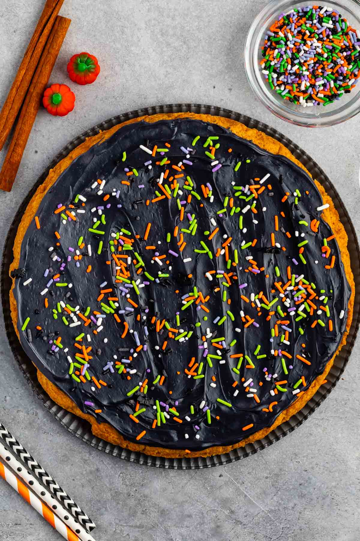 halloween pumpkin cookie cake with black frosting and sprinkles on top.