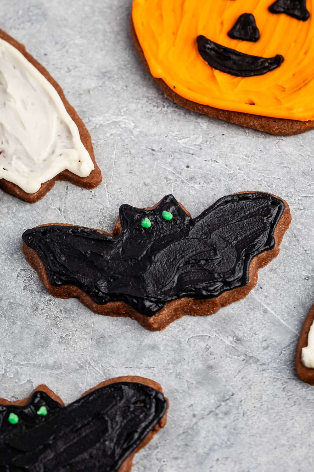 bat shaped cookie with black frosting and green eyes.